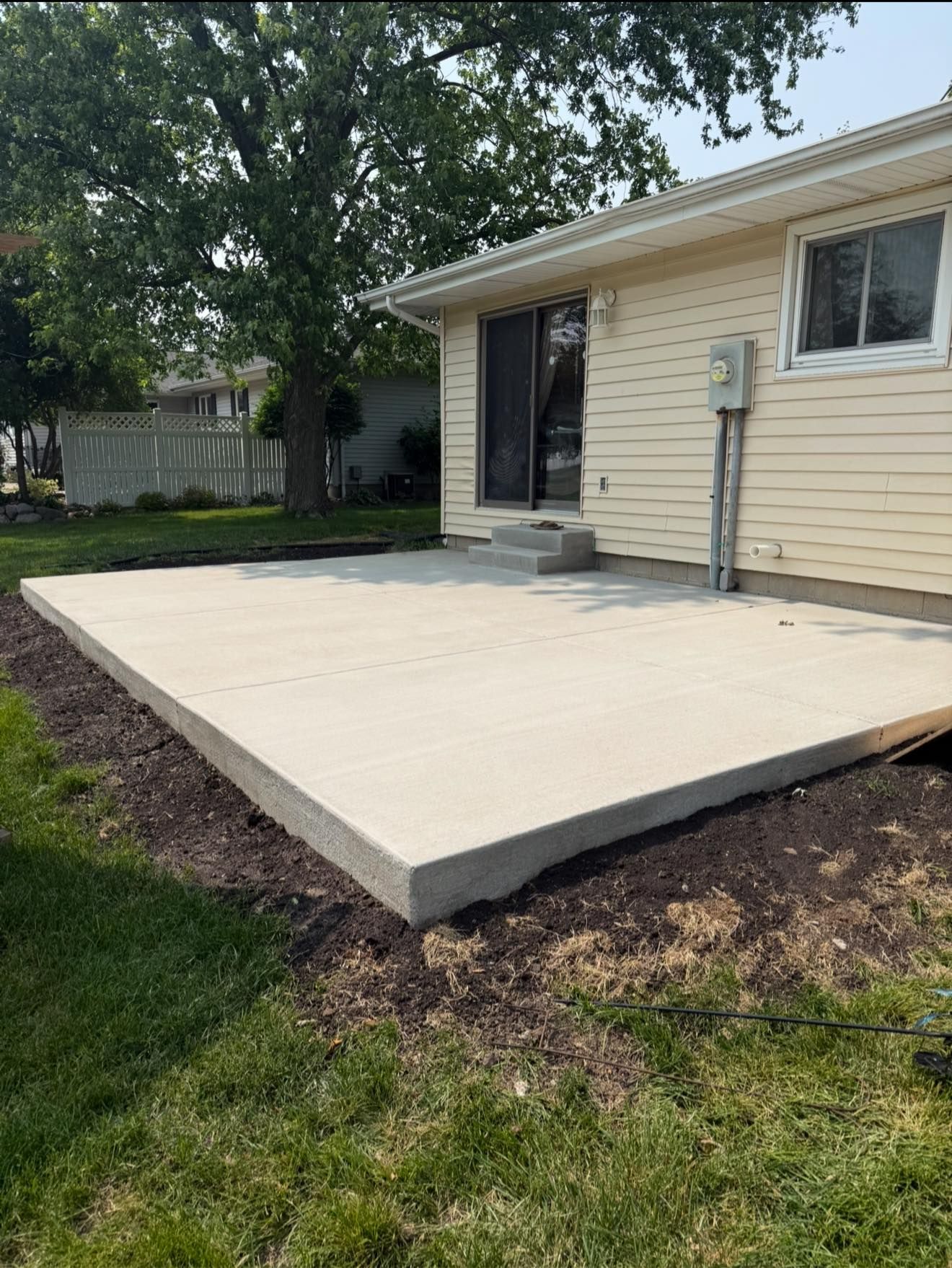 Concrete patio adjacent to a light-colored house with a sliding glass door and a window.