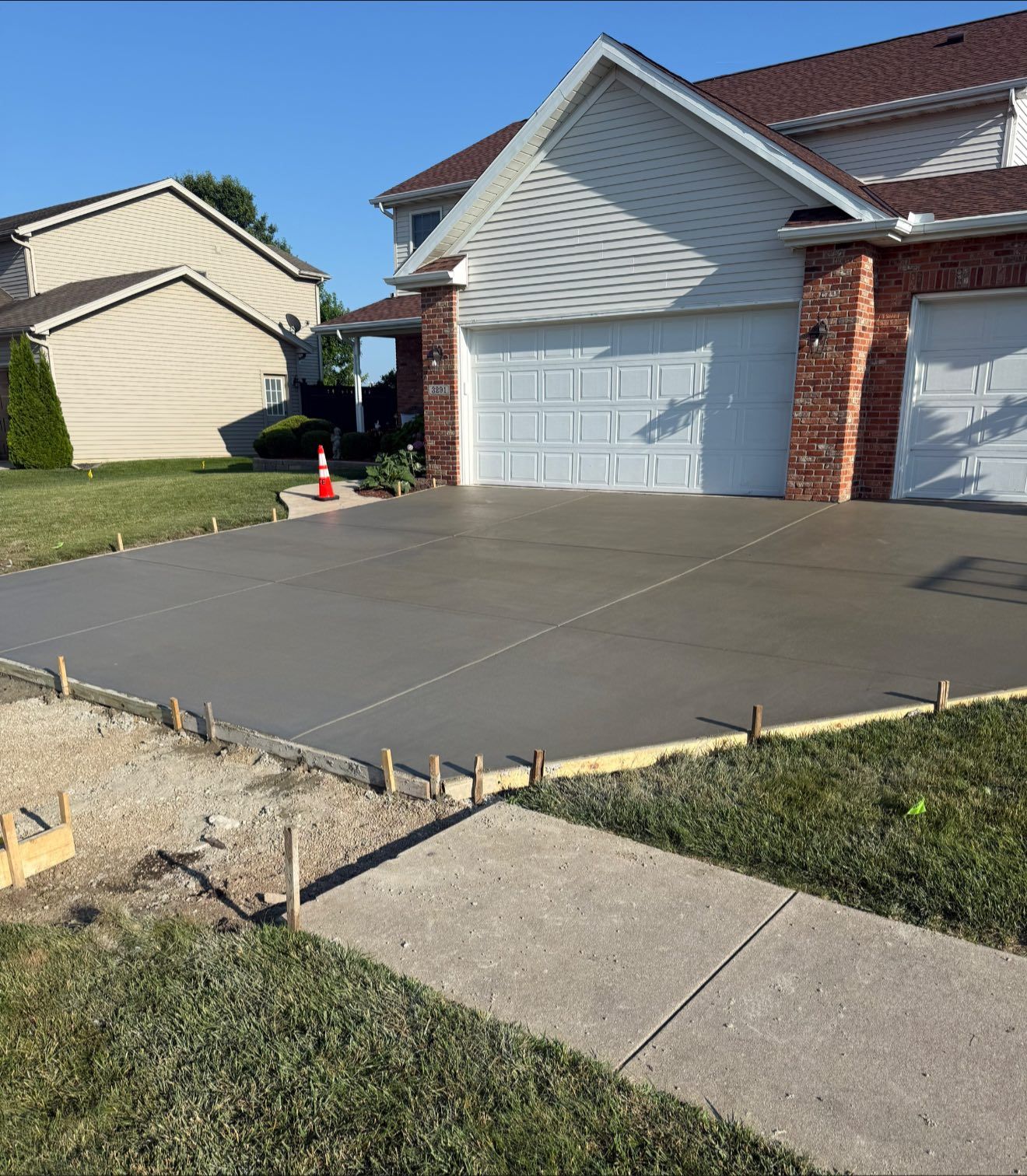 Freshly poured concrete driveway in front of a two-story house with a brick facade and attached garage.