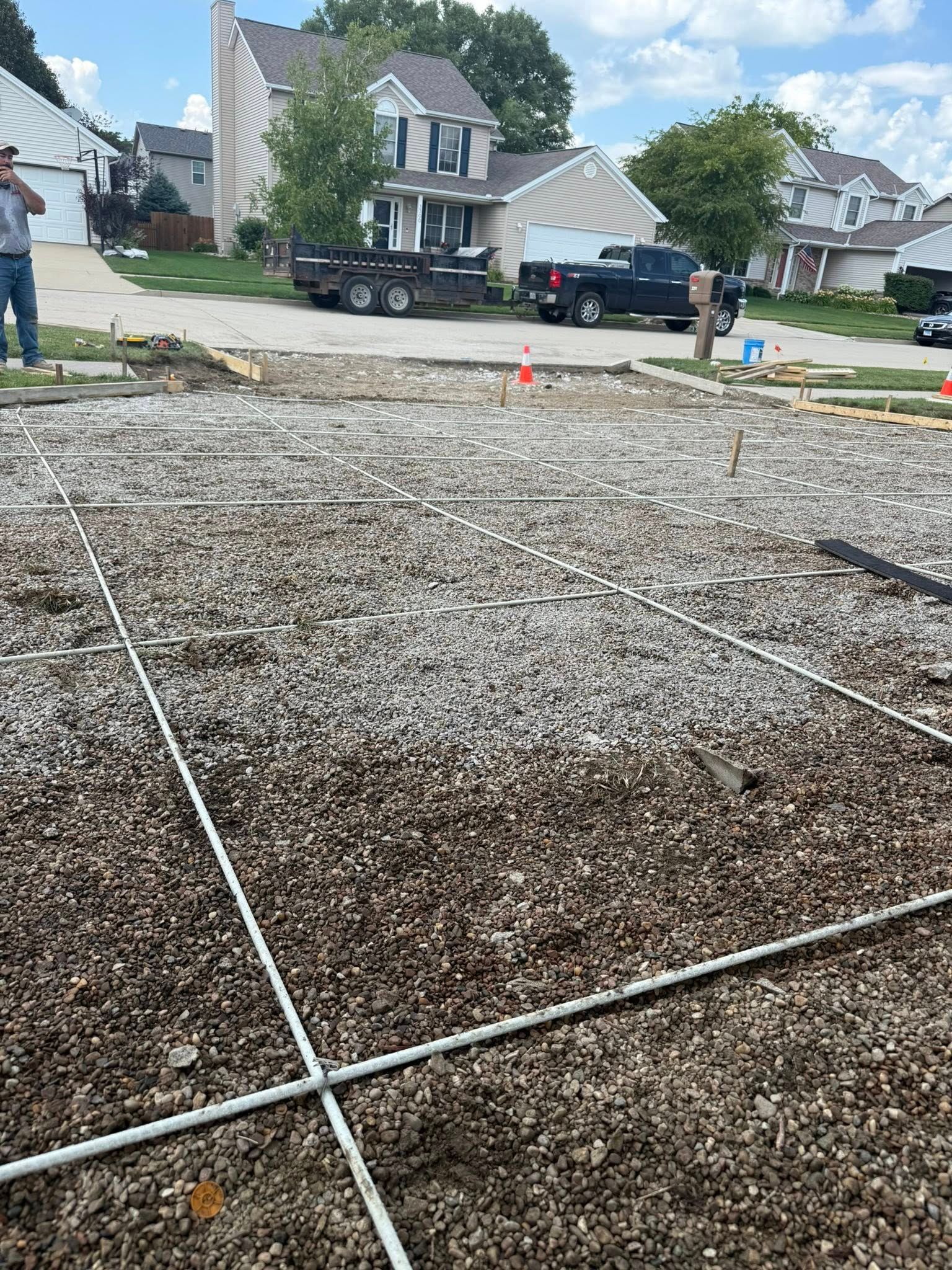 Construction site: gravel base with grid, stakes, and workers in a suburban neighborhood.
