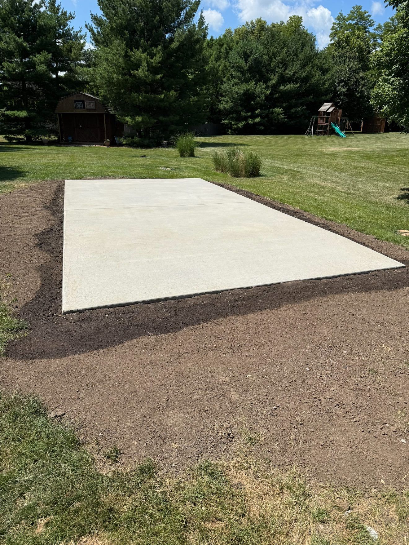 Concrete patio in a grassy backyard, surrounded by dark soil.
