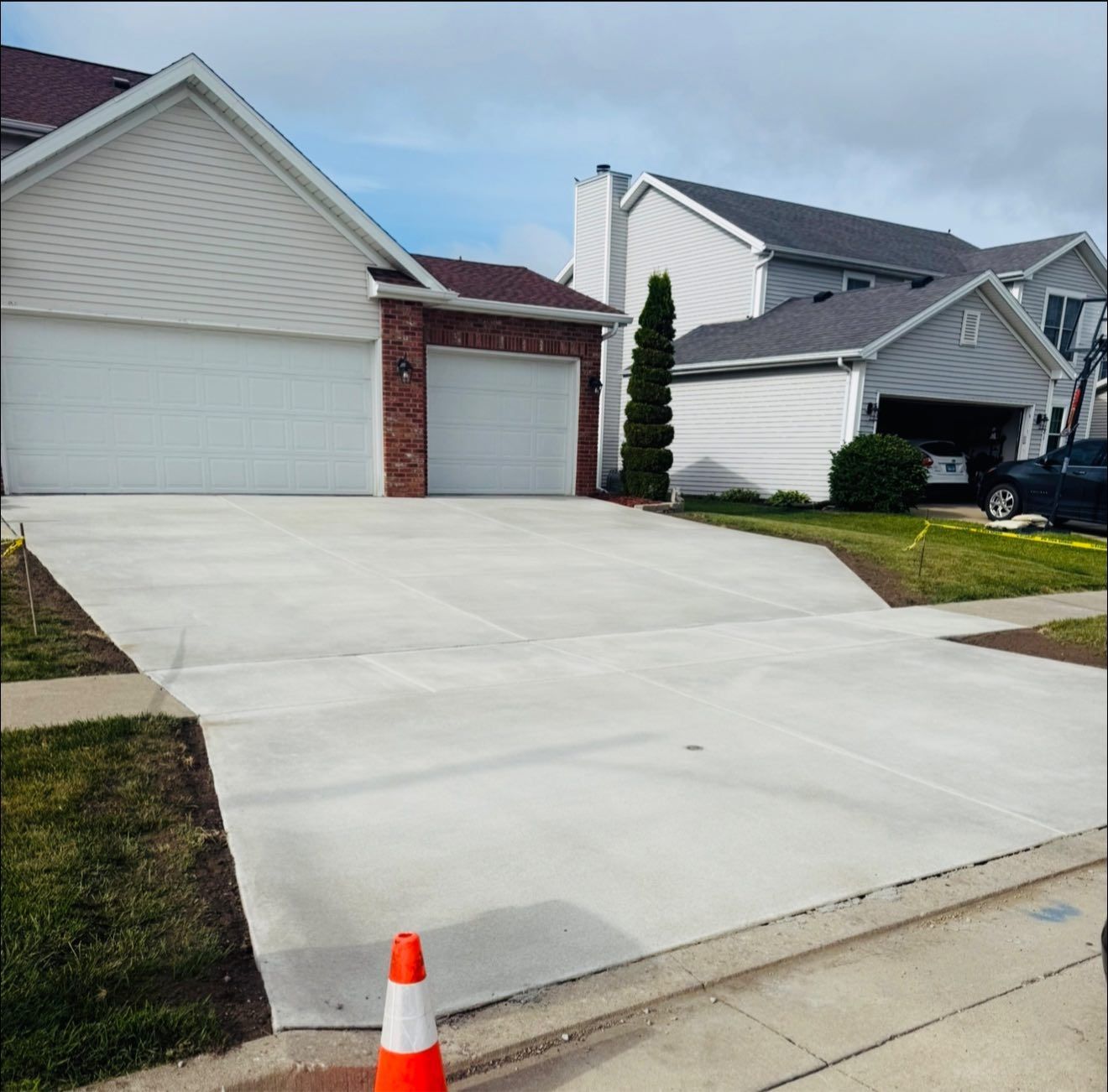 Newly poured concrete driveway in front of a house with attached garage; orange traffic cone in the foreground.