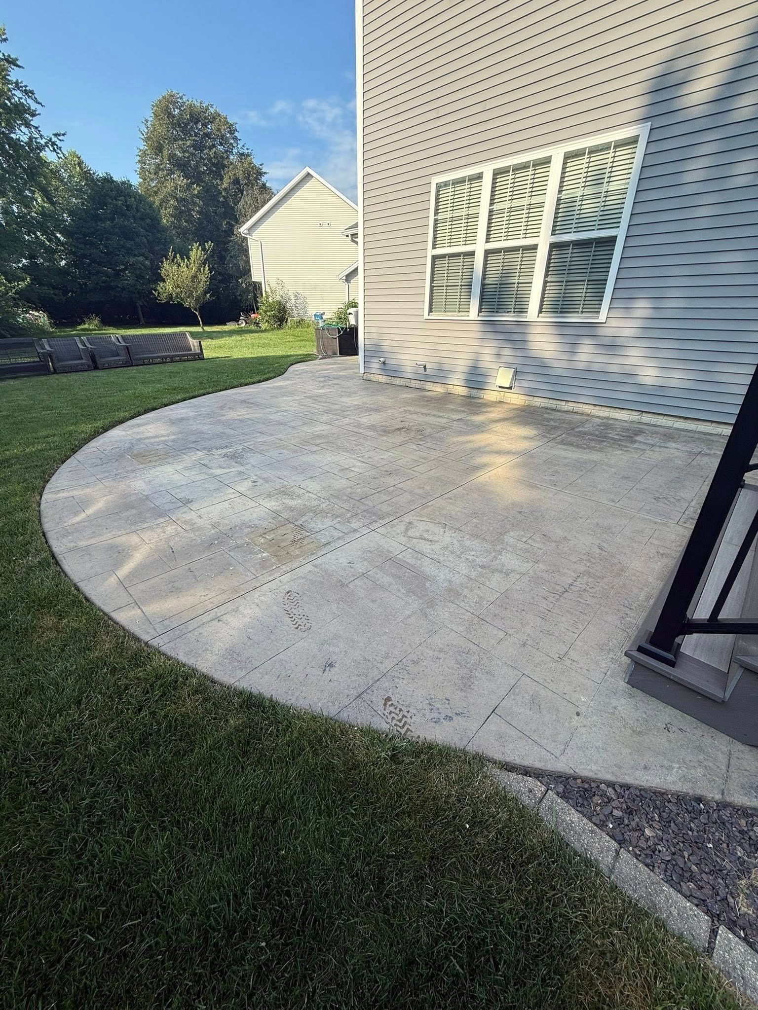 Curved concrete patio next to a house with a window, surrounded by grass.