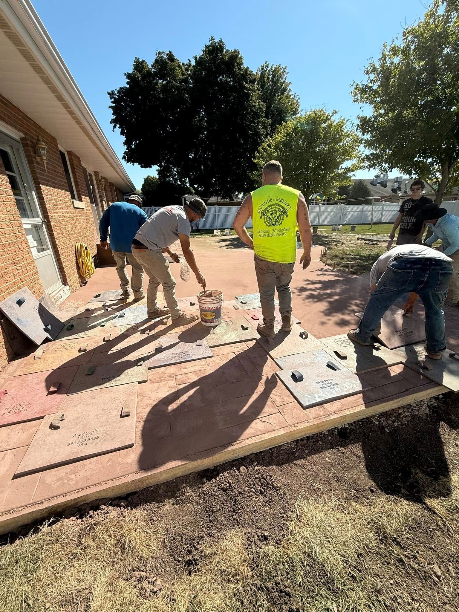 Construction workers installing concrete patio stones. Sunny outdoor setting.