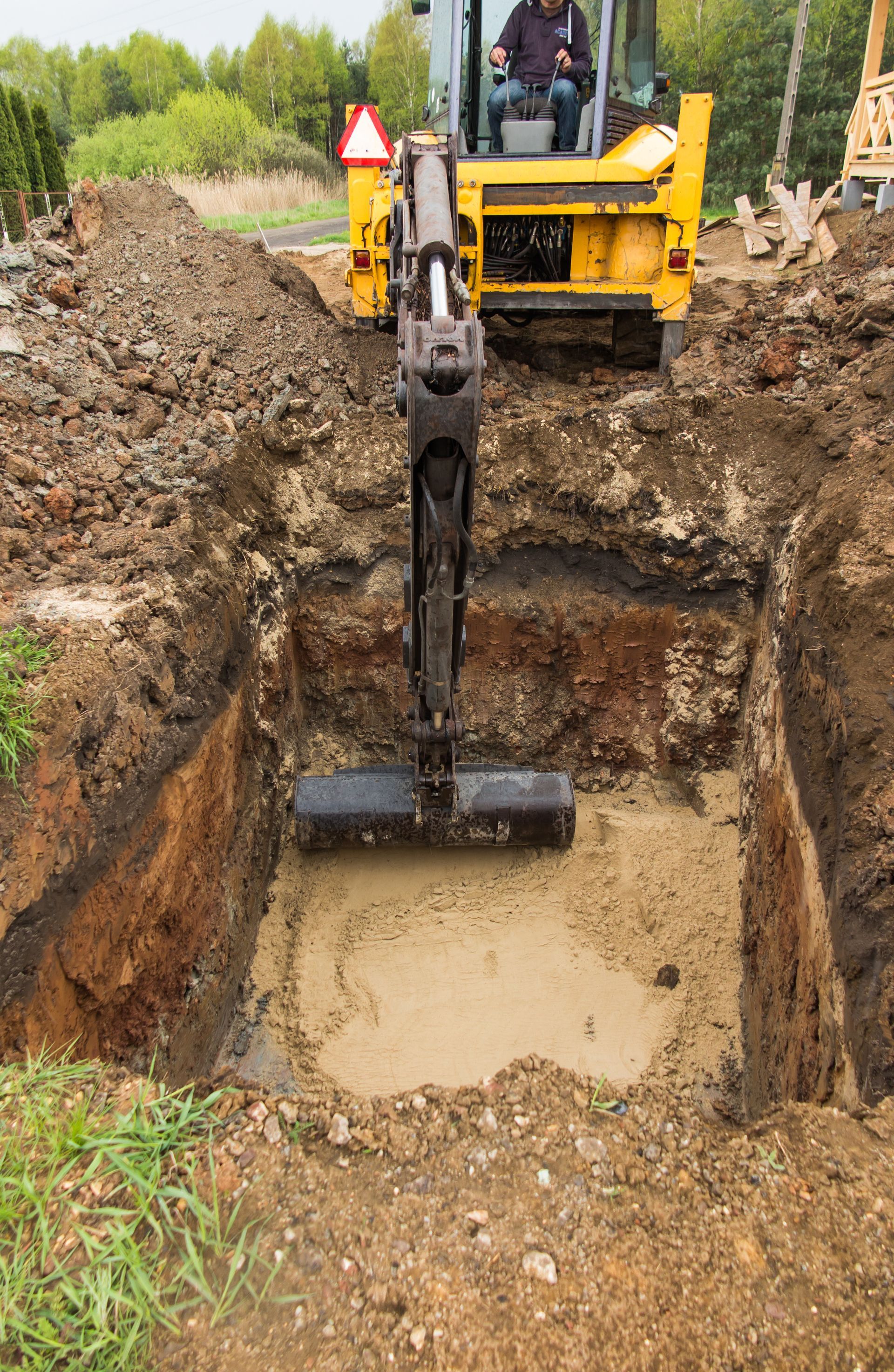 A small excavator digging a square hole in the ground; a person is in the driver's seat.