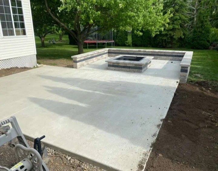 Concrete patio with fire pit and retaining wall in a backyard.