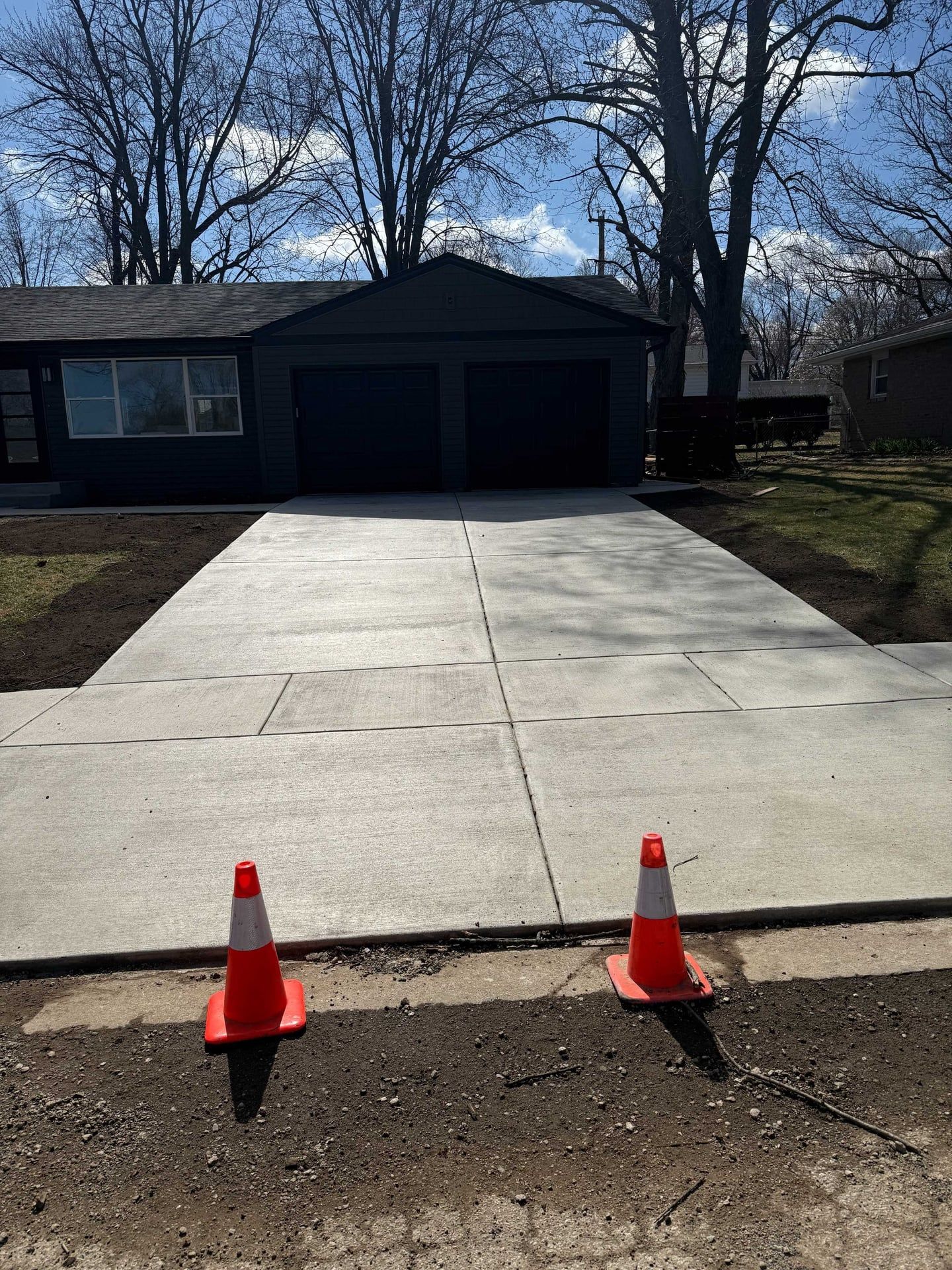 Newly poured concrete driveway with orange safety cones in front of a gray house.
