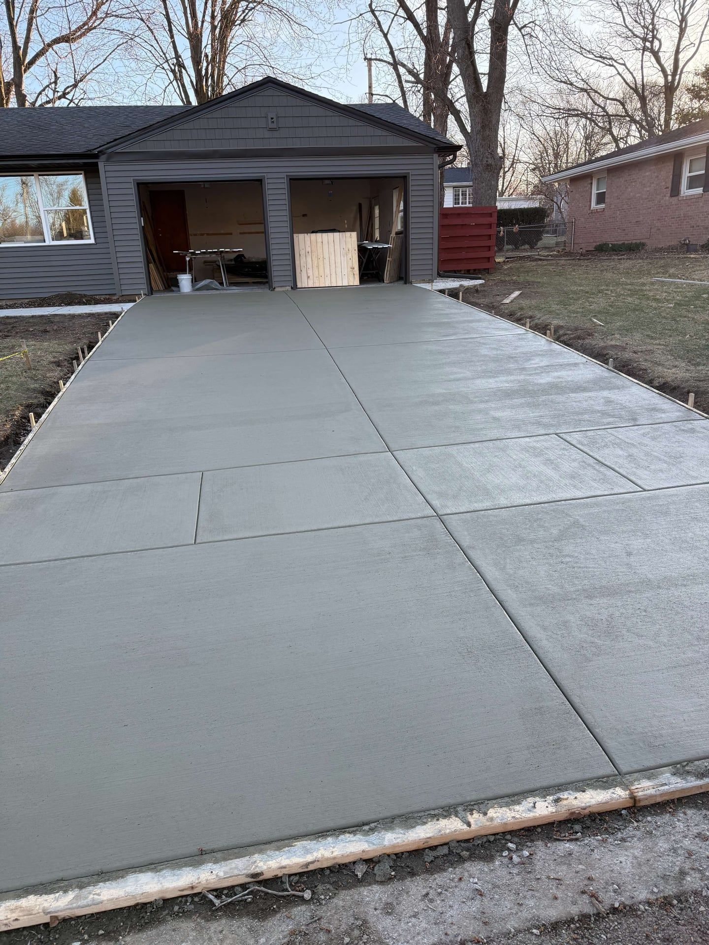 New concrete driveway leading to a gray garage with open door. Gray house in background.