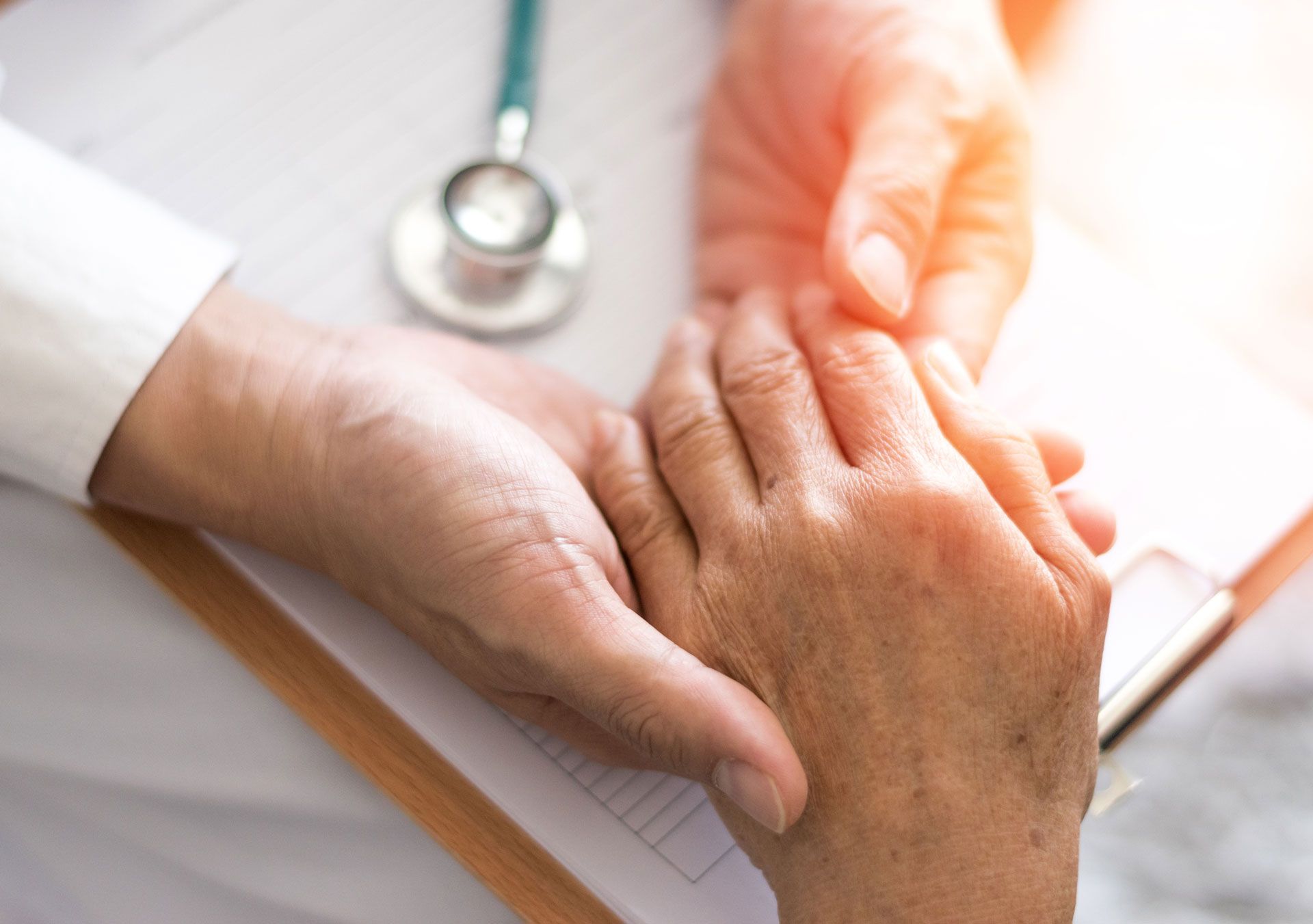 Doctor holding a patient's hand with stethoscope in background.