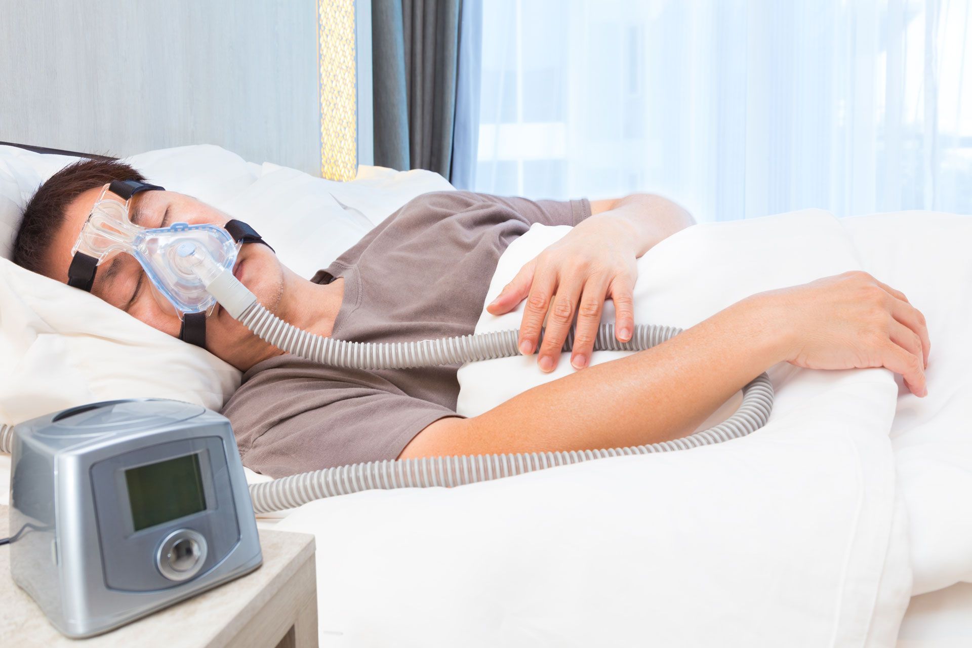 Person sleeping with a CPAP machine and mask in a bedroom.