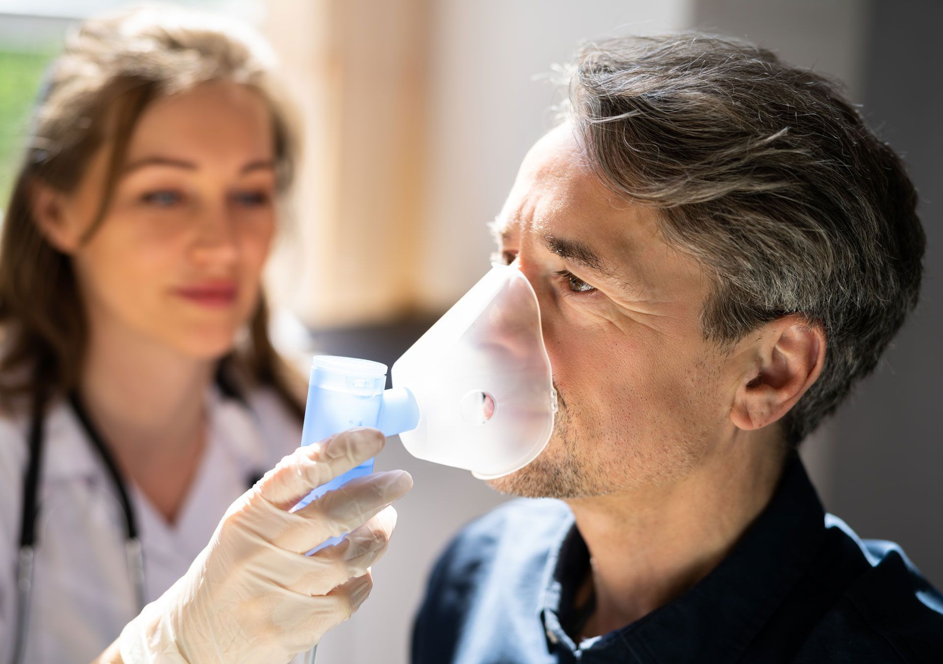 A healthcare worker assists a patient with an oxygen mask indoors.
