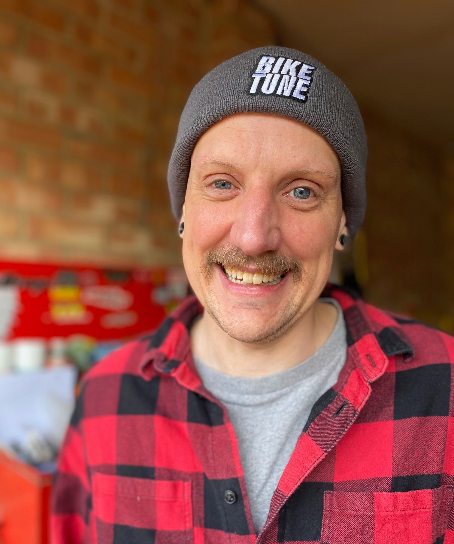 A man wearing a beanie and a plaid shirt is smiling.