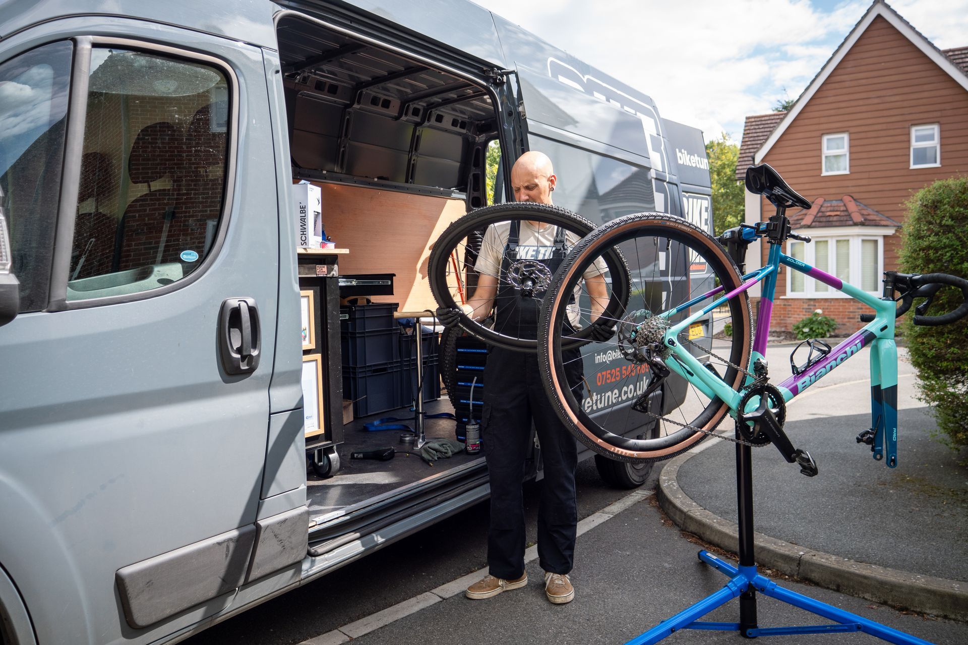 Man repairing a bicycle in front of a van with its doors open.