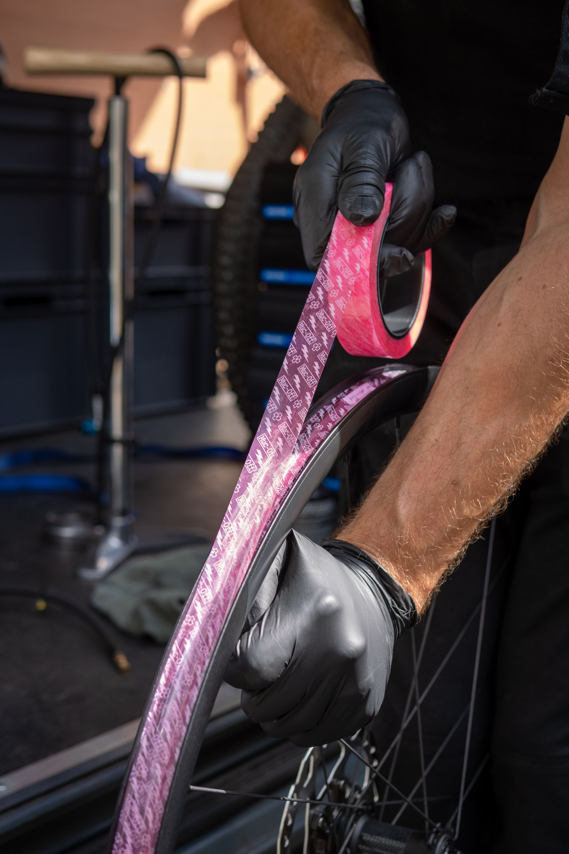 Person in black gloves applying pink glittery rim tape to a bicycle wheel.