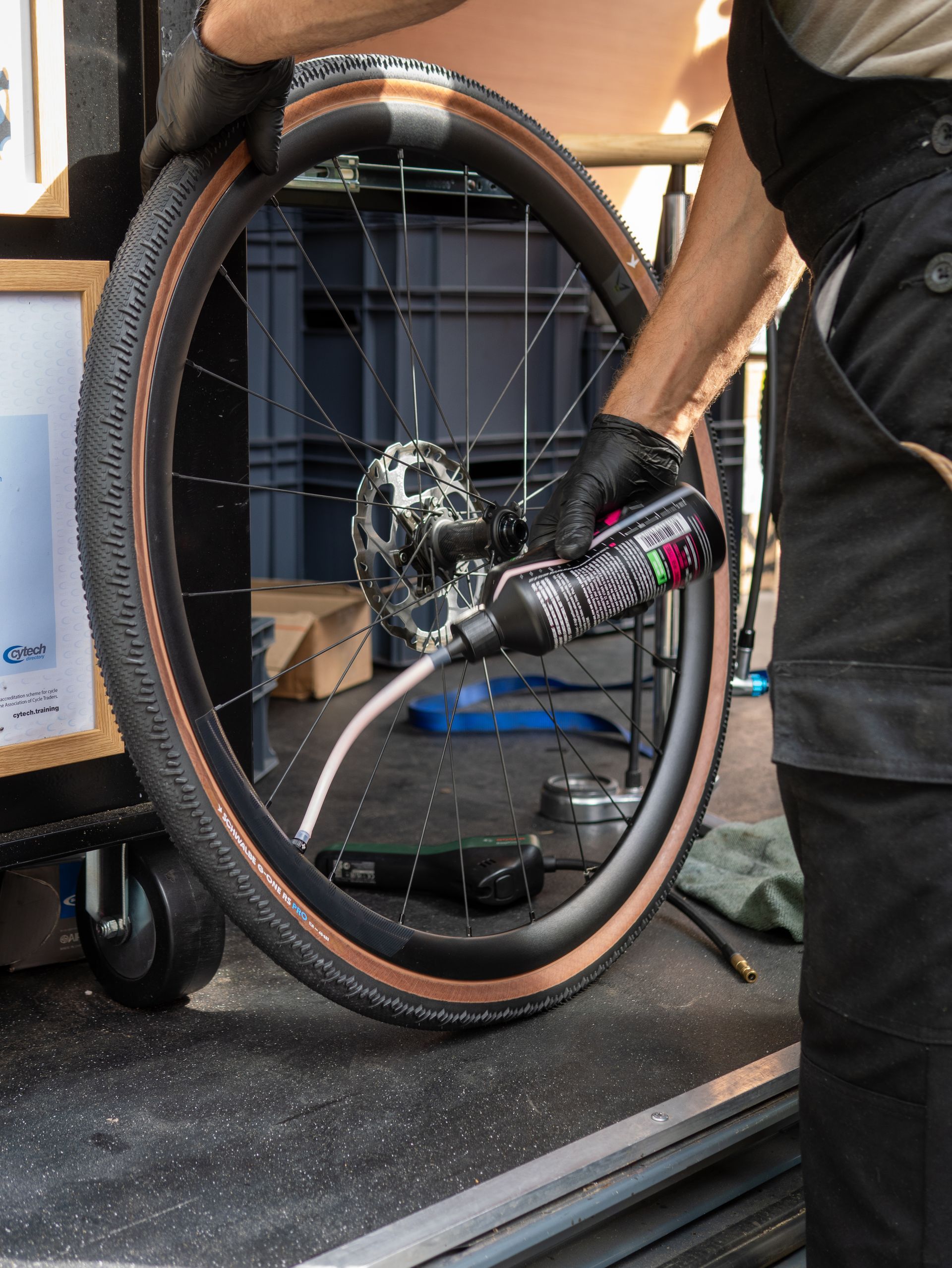 Person adding sealant to a bicycle tire, wearing black gloves, indoors.