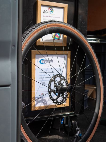 Bike wheel mounted, in front of framed certificates; brown tire, black brake rotor, black spokes.