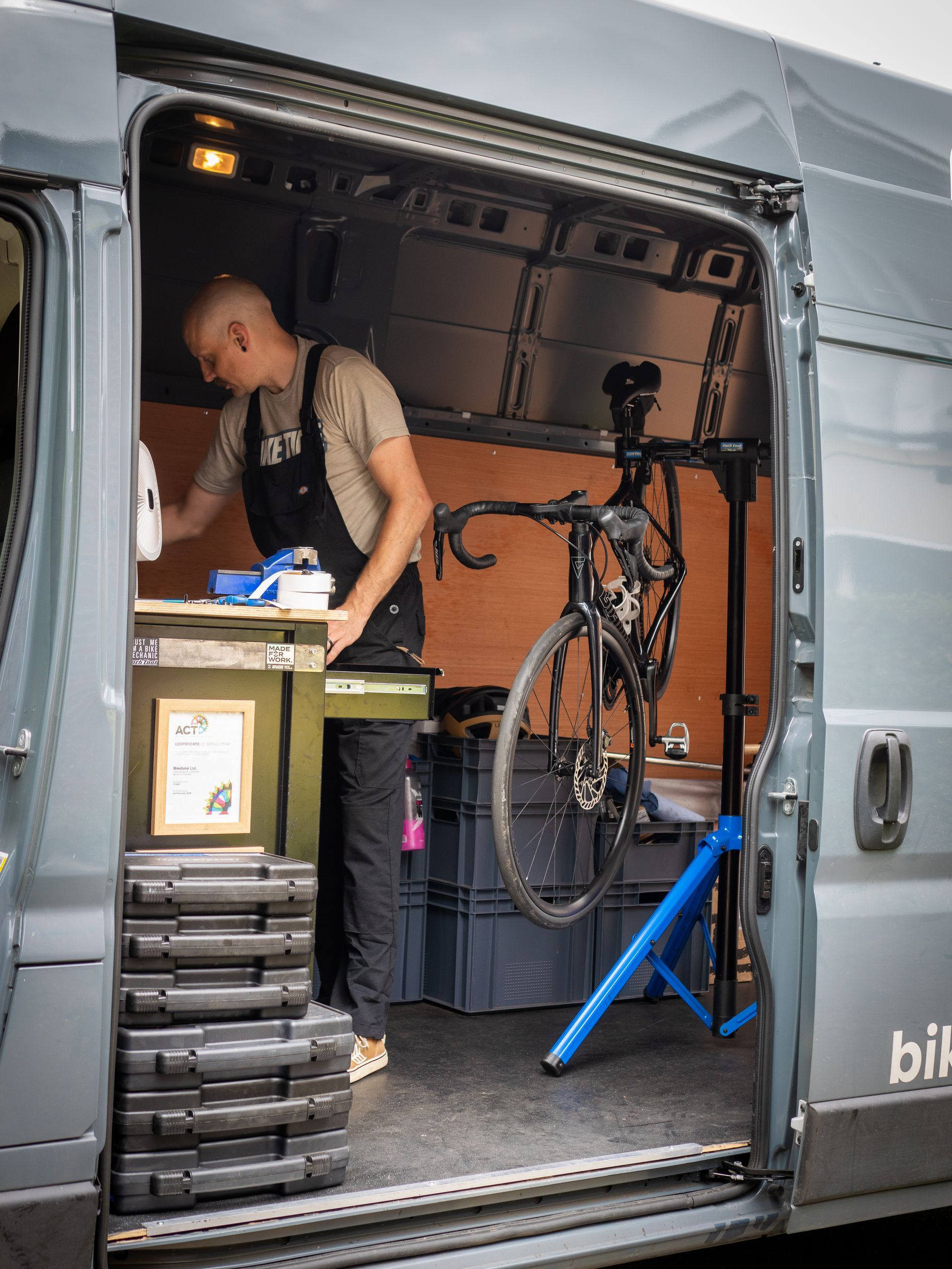 Man in van repairing a bicycle. Gray van interior with repair stand.