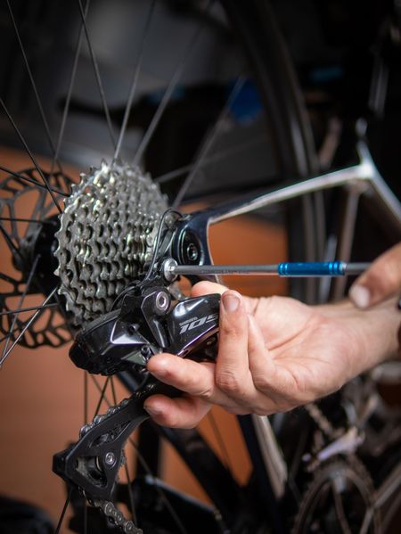 Person using a screwdriver to adjust a bicycle's rear derailleur.