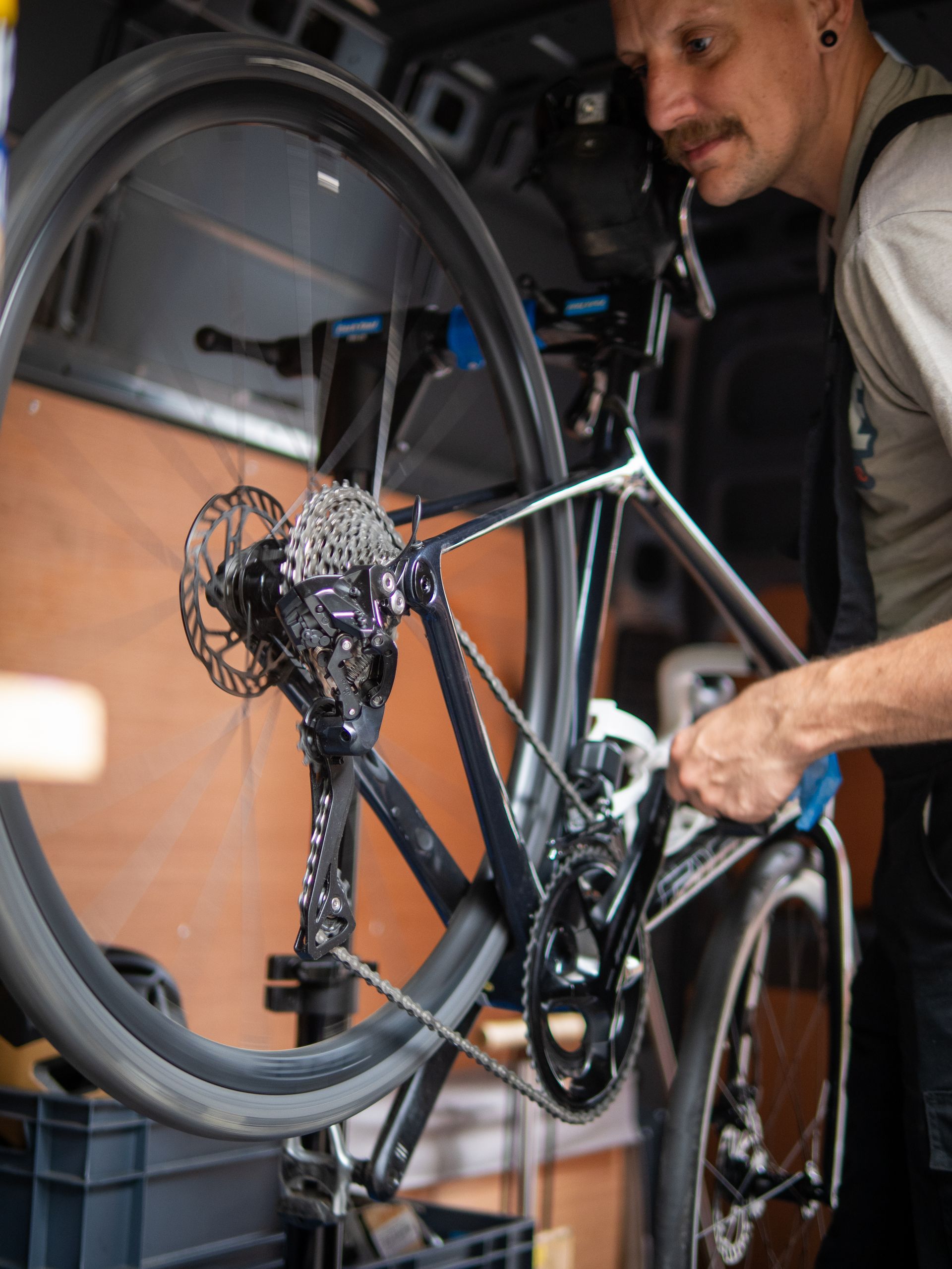 Man fixing a bicycle in a van. Dark bike with silver details, man wears work clothes and has a mustache.