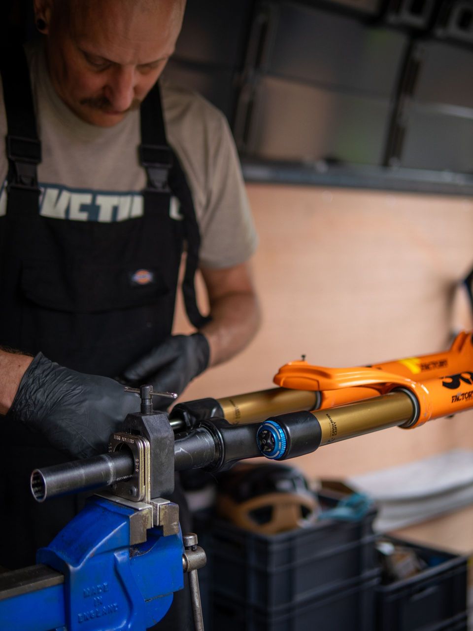 Mechanic working on a bicycle fork in a van, wearing black gloves. Blue vice holds the fork, gold and blue.