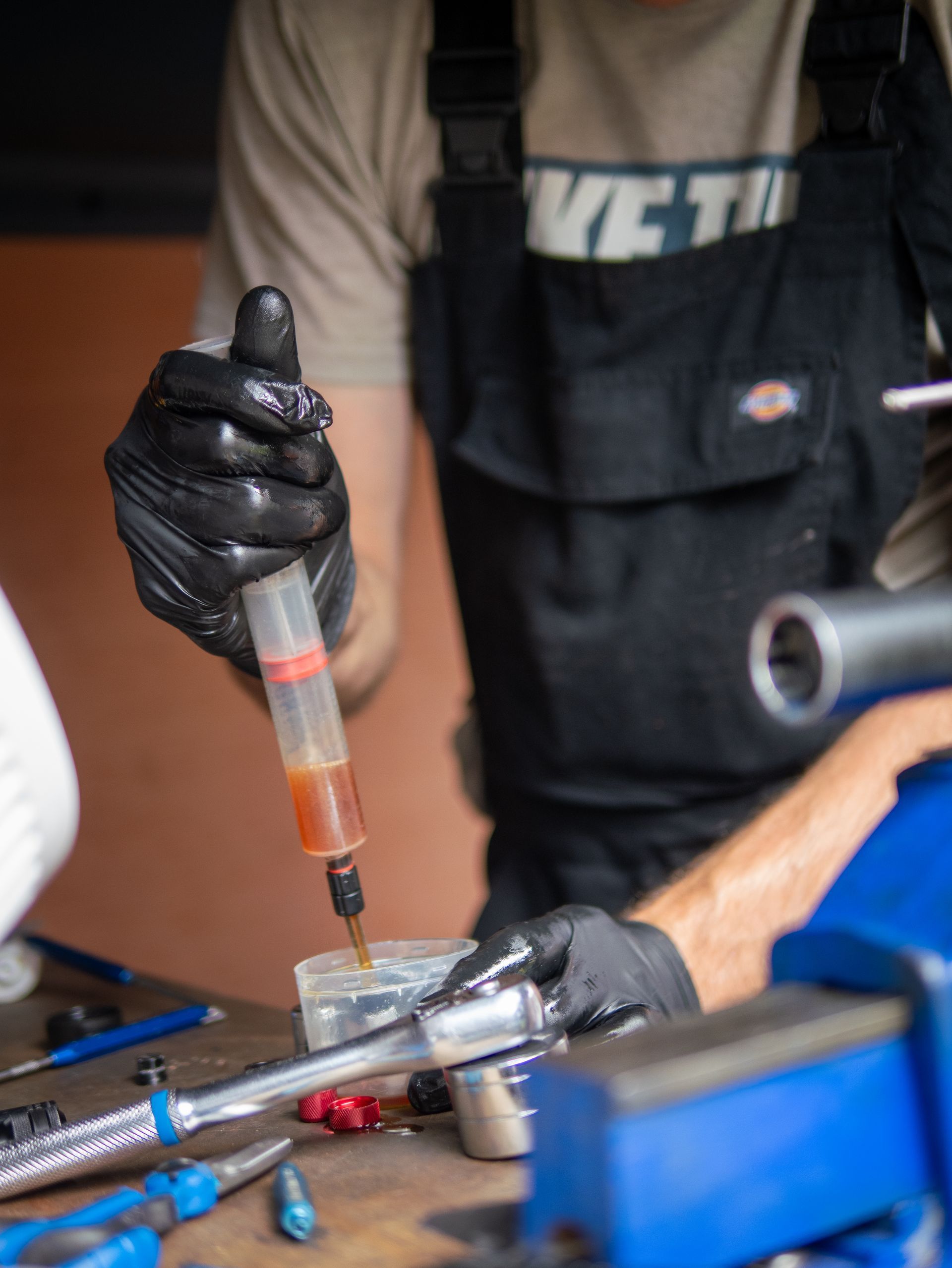 Person in black gloves filling a suspension fork with oil using a syringe. Workshop setting.