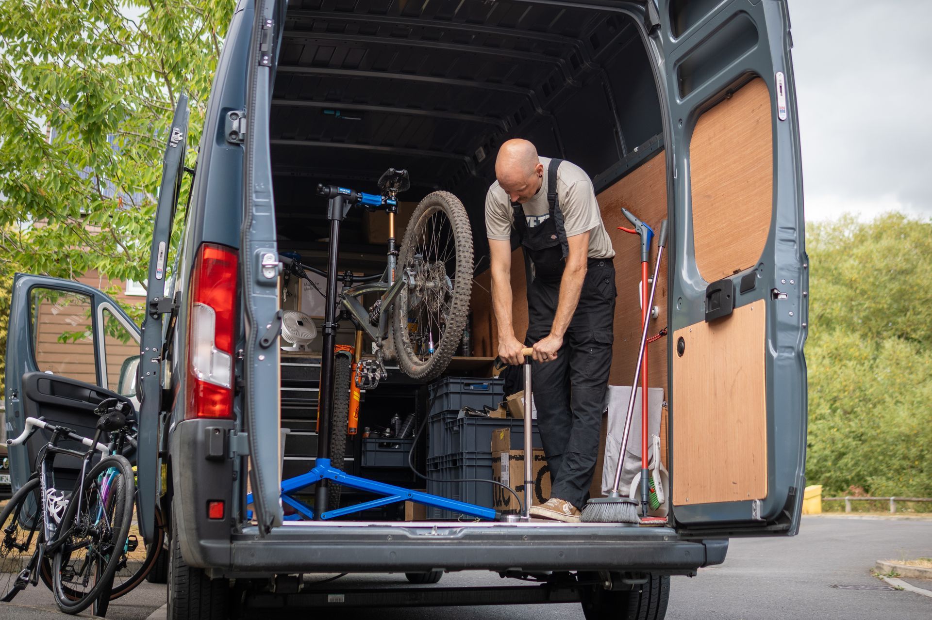 A man fixing a mountain bike inside a van, with a bike repair stand and tools visible.
