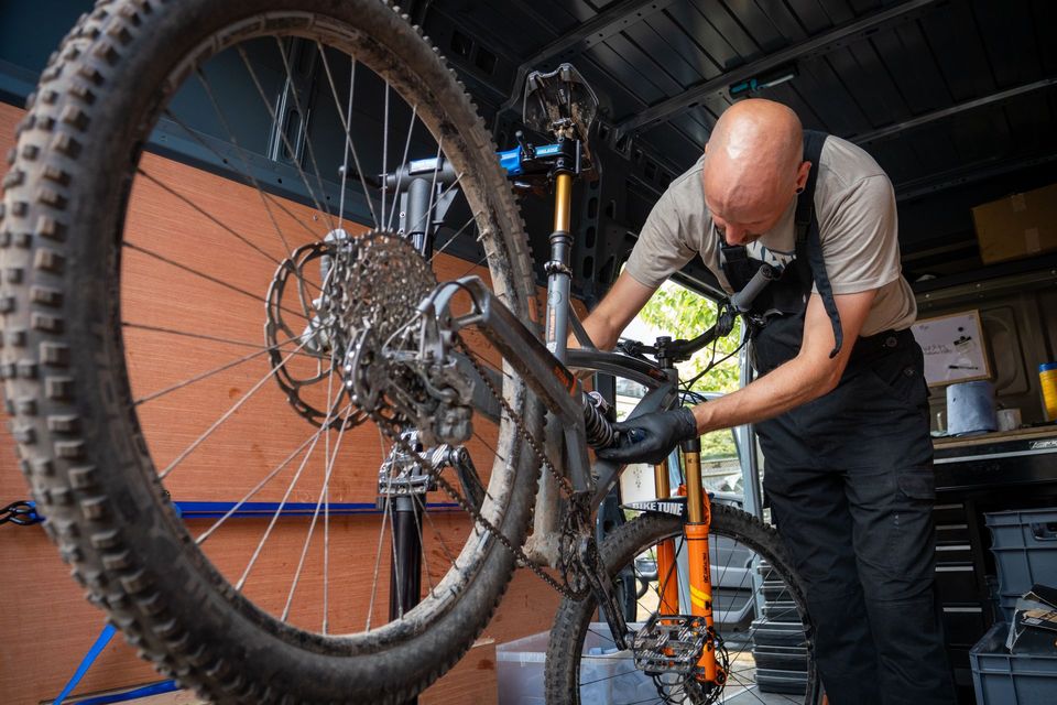 Man working on a mountain bike in a garage, wearing black gloves.