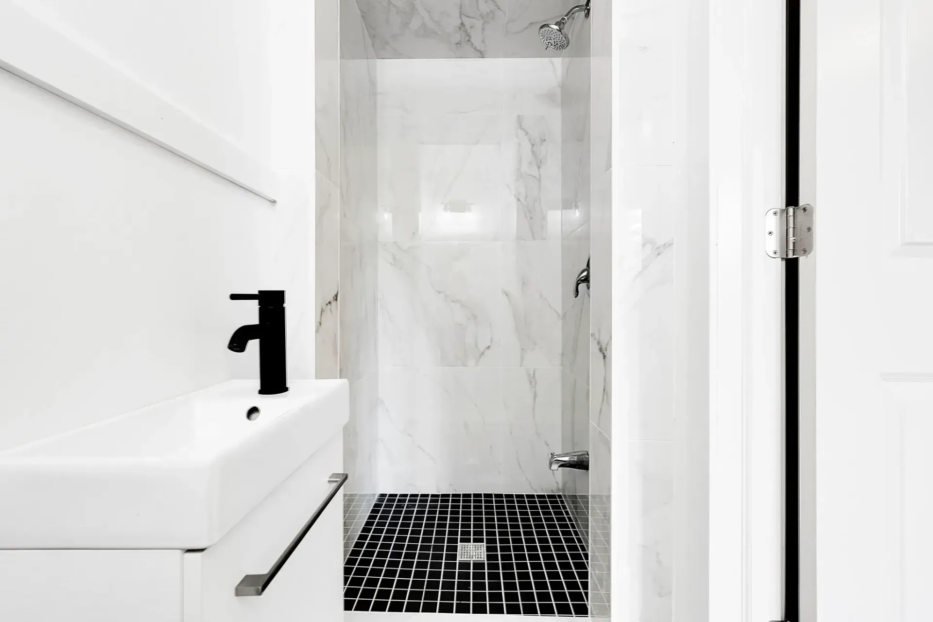 Modern 3-piece bathroom featuring a black tile floor, marble shower walls, and a sleek black faucet with minimalist white vanity.Design by 17 Plumbing team
