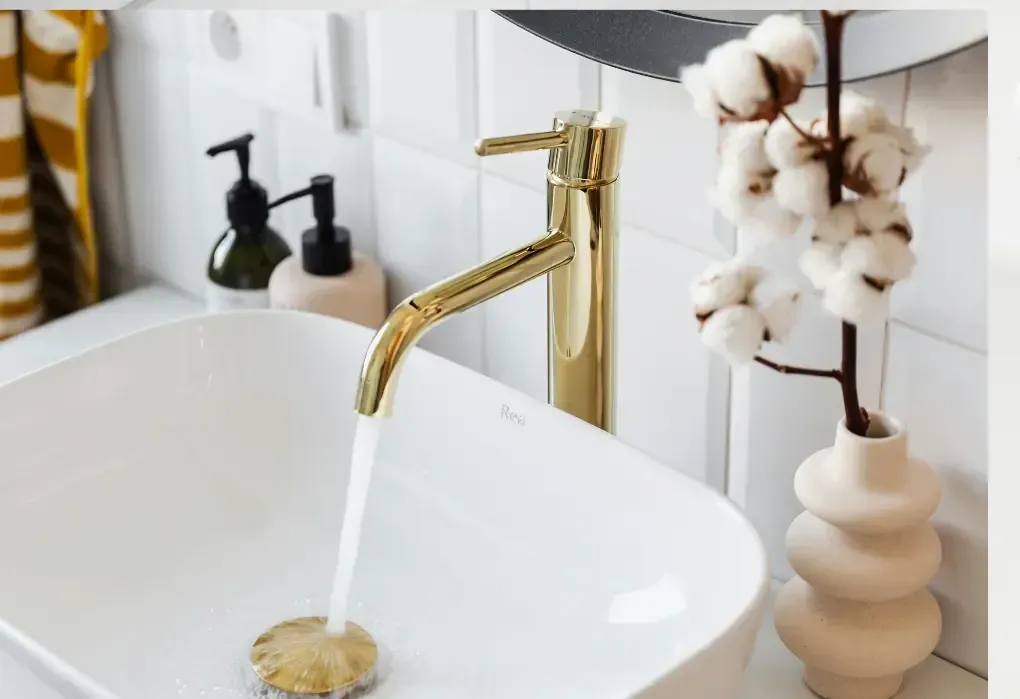 Gold faucet with running water over a white sink. Cotton branch in a beige vase sits to the right, installed by 17 Plumbing & Construction design in Oakville