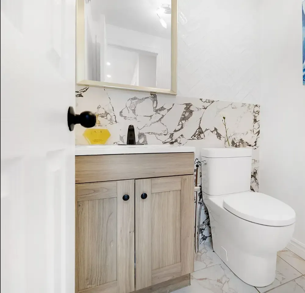 Luxury powder room makeover with new marble backsplash tiles, wooden vanity, premium toilet, and framed mirror.