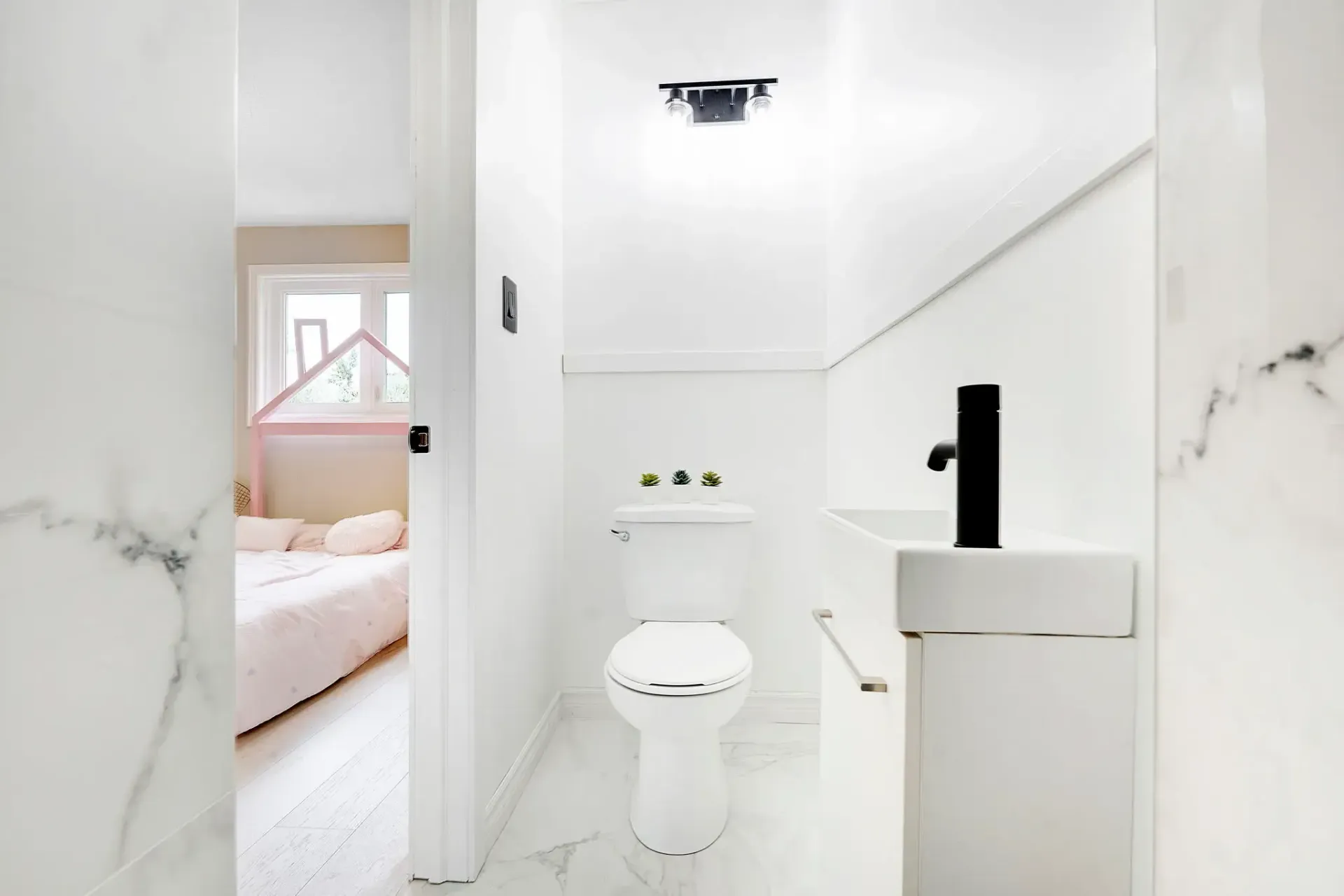 Compact white bathroom renovation with premium toilet, black faucet, white vanity, and polished marble flooring.