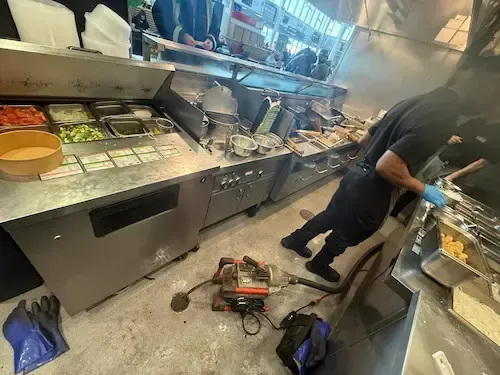 Emergency drain cleaning in Oakville commercial kitchen using professional equipment to clear blocked floor drain