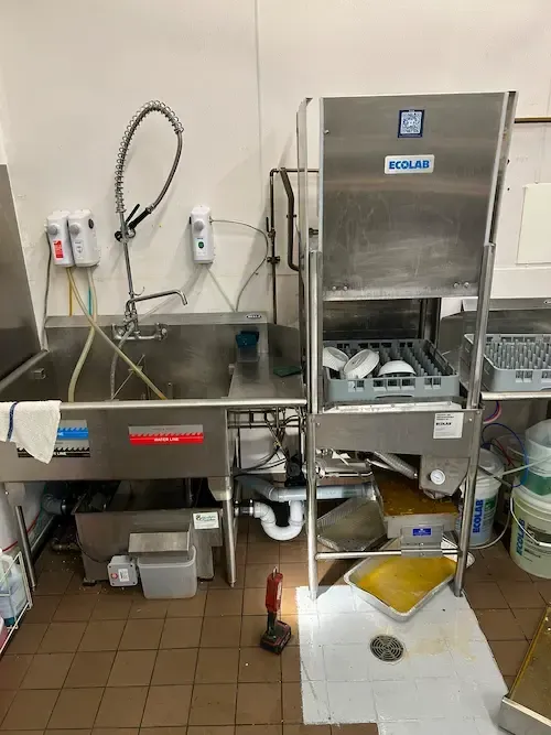 Powerflushing drain cleaning service at an Oakville commercial kitchen, showing a grease trap backup under a dishwasher caught in foil pans.