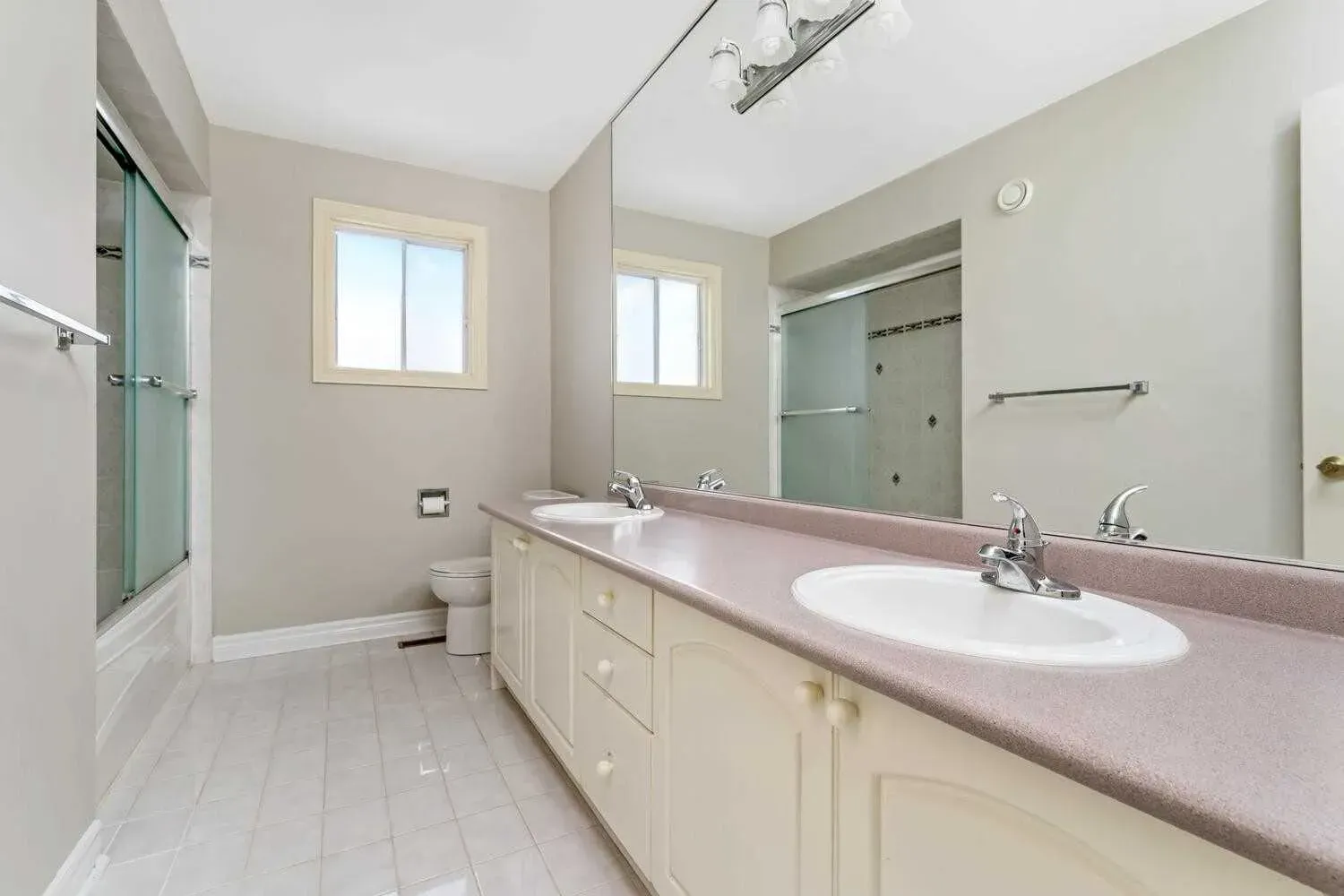A bathroom with two sinks , a toilet , and a large mirror.