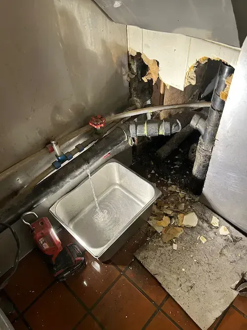 Pipe leak under restaurant kitchen sink in Oakville showing active water damage and leak investigation work