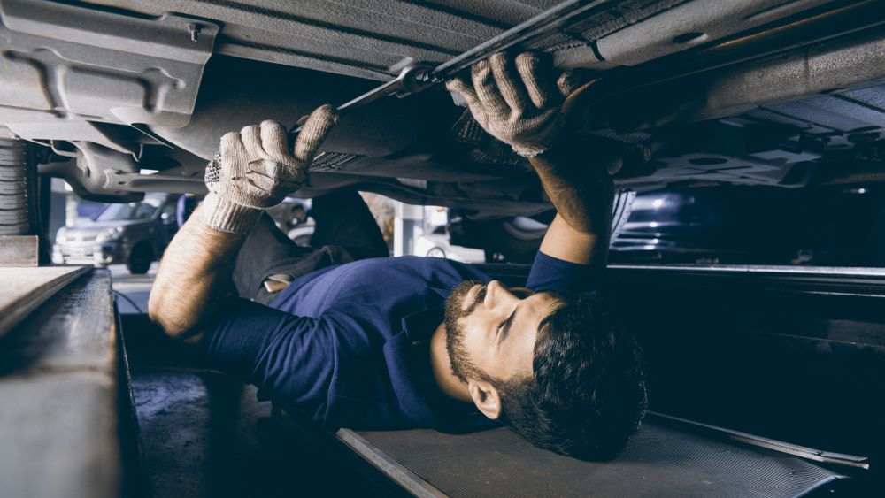 A Man Is Laying On His Back Under A Car In A Garage — Loch’s Garage In Emerald, QLD