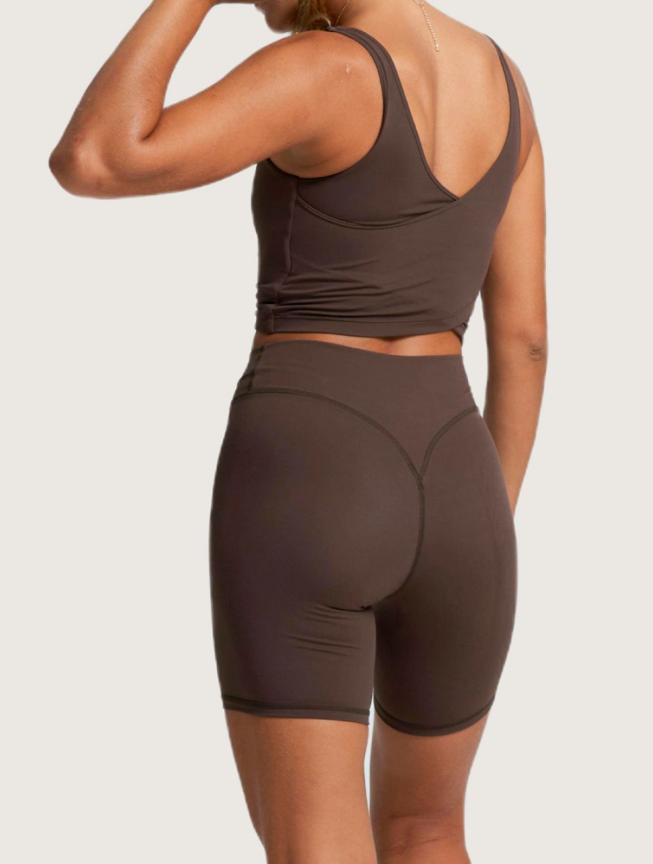 Una persona vista de espaldas, vestida con una camiseta sin mangas ajustada de color marrón chocolate y unos pantalones cortos de ciclista de talle alto a juego.
