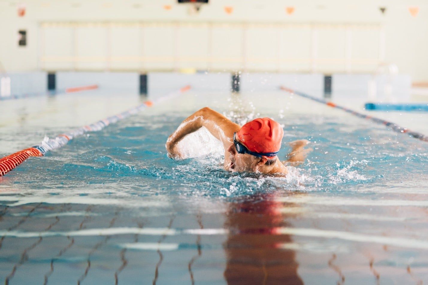 Man is Swimming in a Swimming Pool Wearing a Red Cap and Goggles — Care FNQ Pty Ltd in Cairns City, QLD