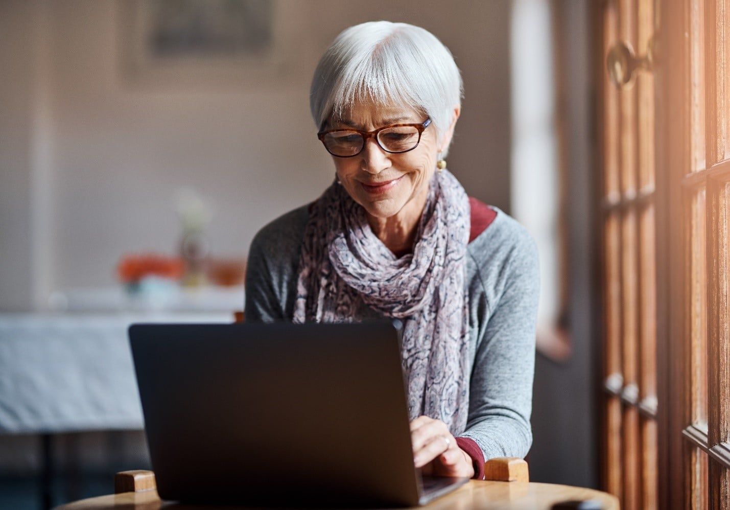 Elderly Woman is Sitting at a Table Using a Laptop Computer — Care FNQ Pty Ltd in Cairns City, QLD