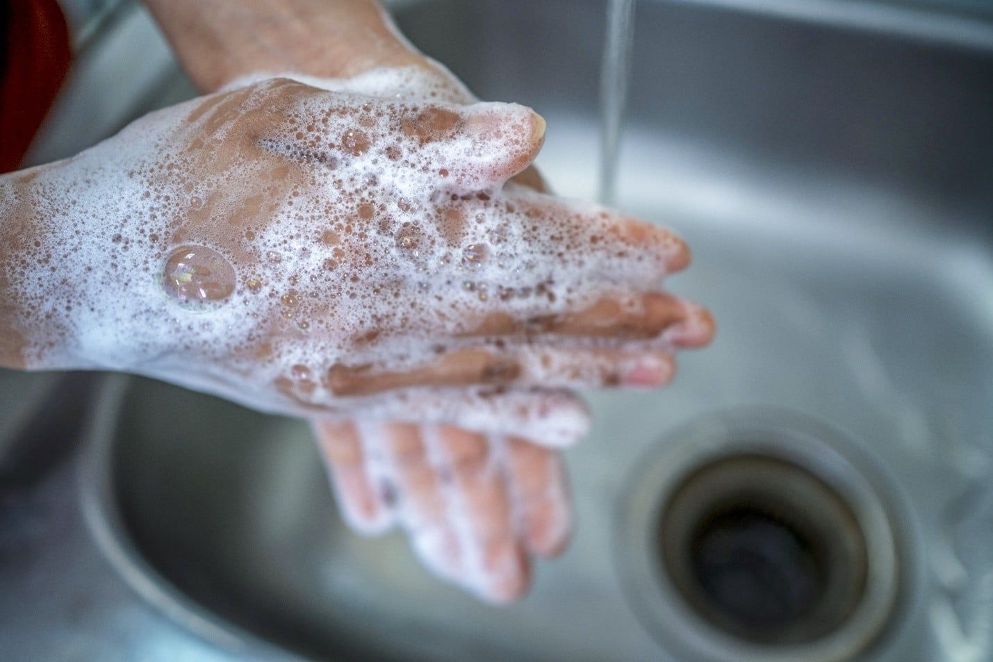 Person is Washing Their Hands in a Sink With Soap and Water — Care FNQ Pty Ltd in Cairns City, QLD