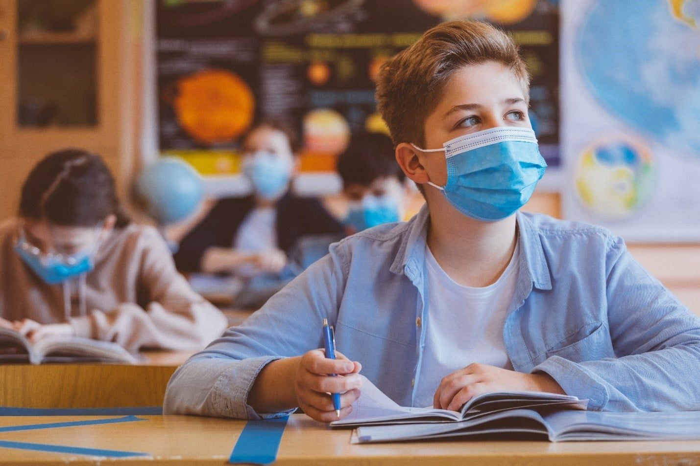 Boy Wearing a Face Mask is Sitting at a Desk in a Classroom — Care FNQ Pty Ltd in Cairns City, QLD