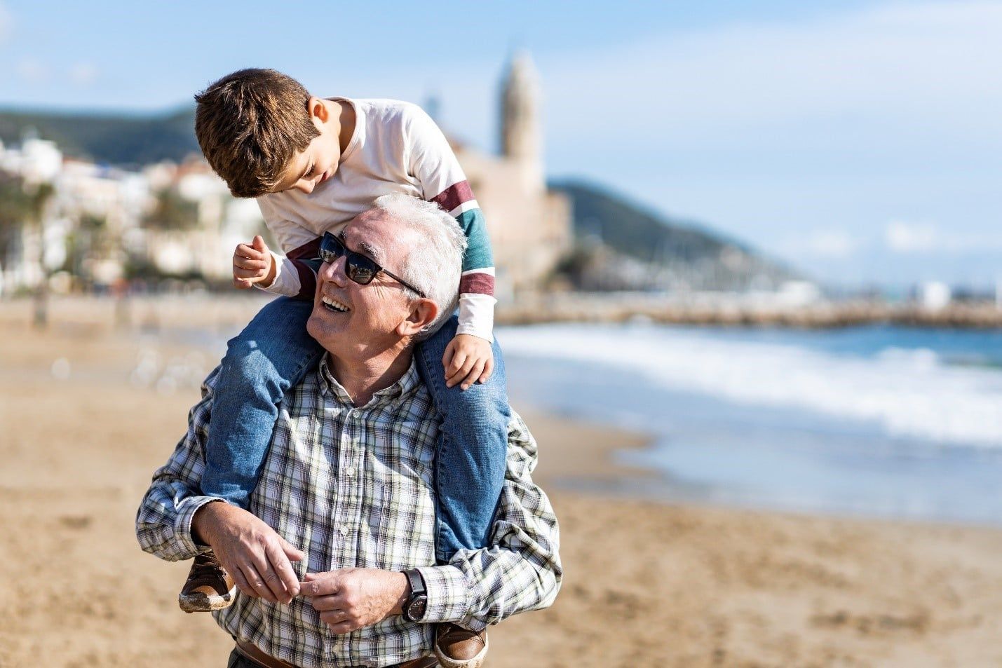 Elderly Man is Carrying a Young Boy on His Shoulders on the Beach — Care FNQ Pty Ltd in Cairns City, QLD