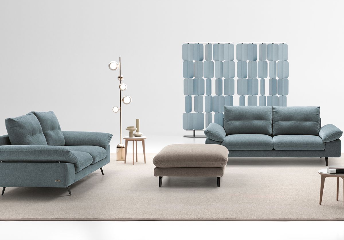 Un soggiorno con due divani, un pouf e una lampada.