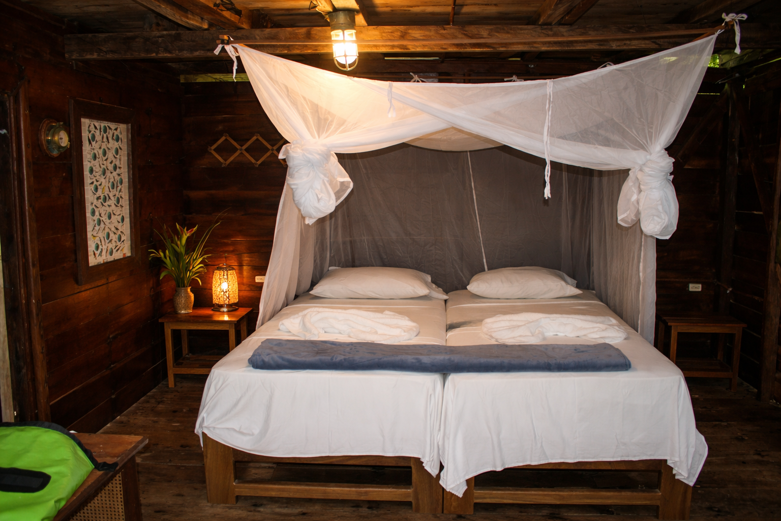 Dormitorio con dos camas, mosquitero blanco, paredes revestidas de madera, mesitas de noche y linterna.