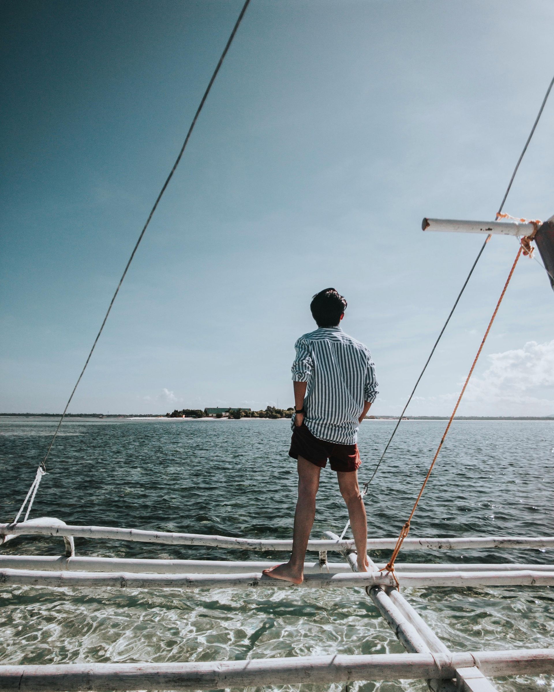 Person standing on a boat, looking out at the ocean under a clear blue sky.