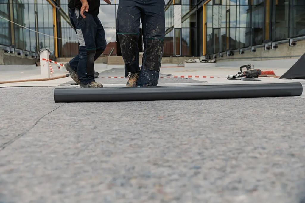 A man is rolling a roll of carpet on a roof.