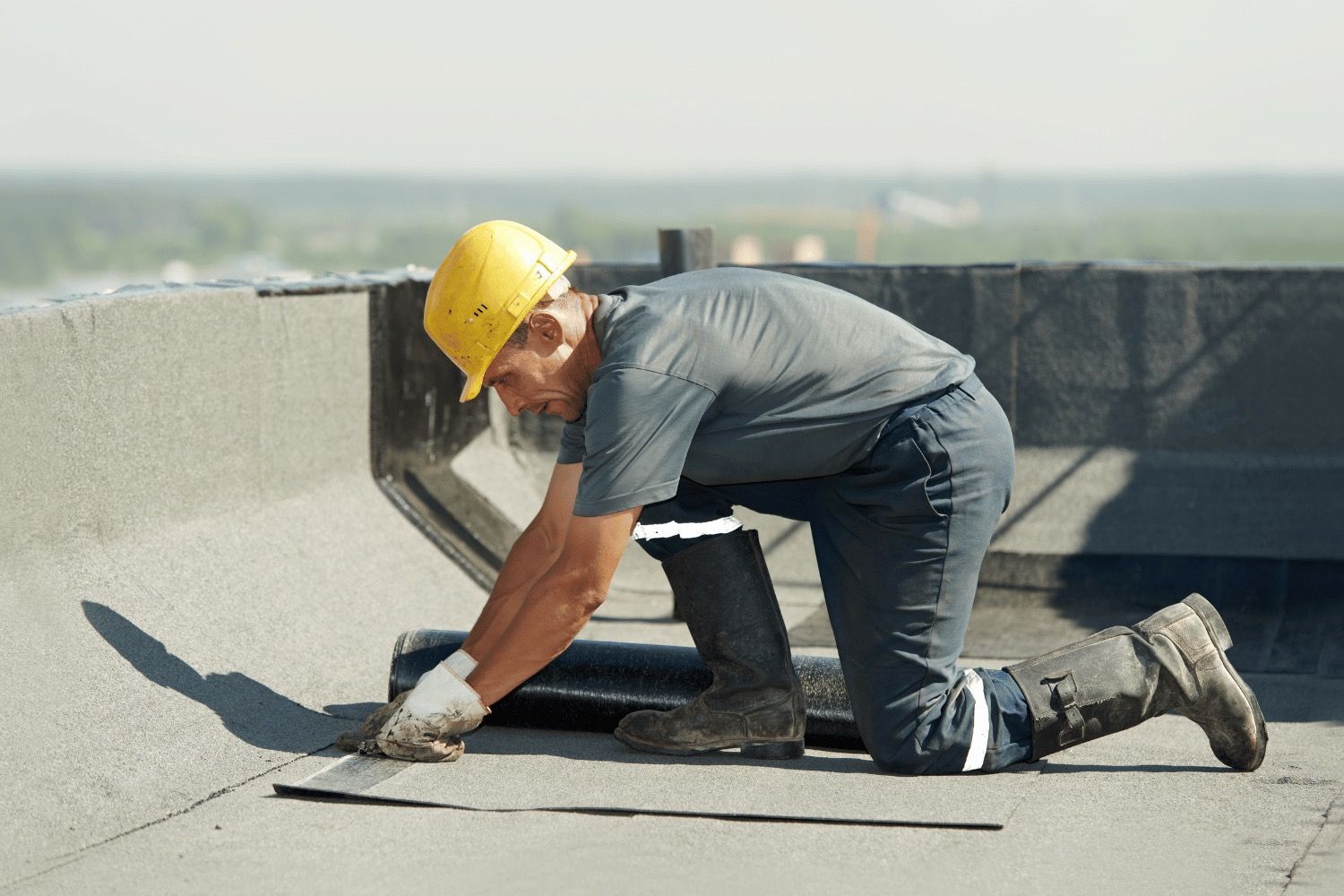 A man wearing a hard hat is kneeling down on a roof.