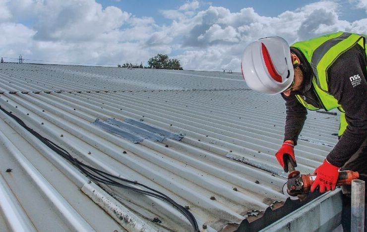 A man wearing a hard hat and safety vest is working on a roof.