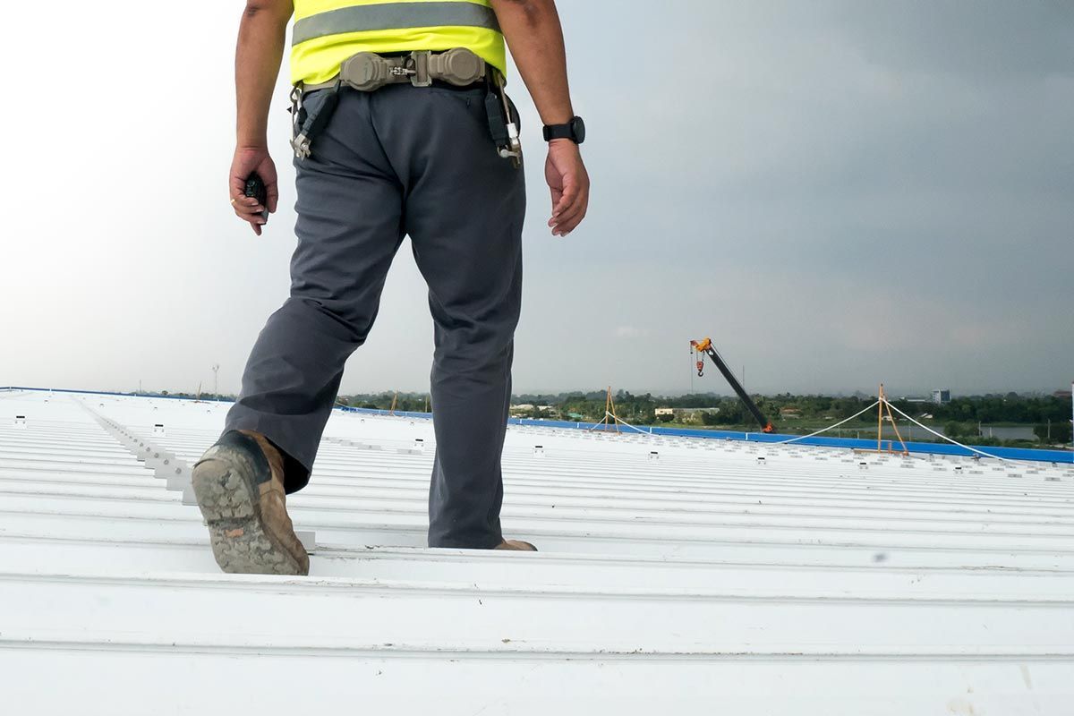 A construction worker is walking on a white roof.