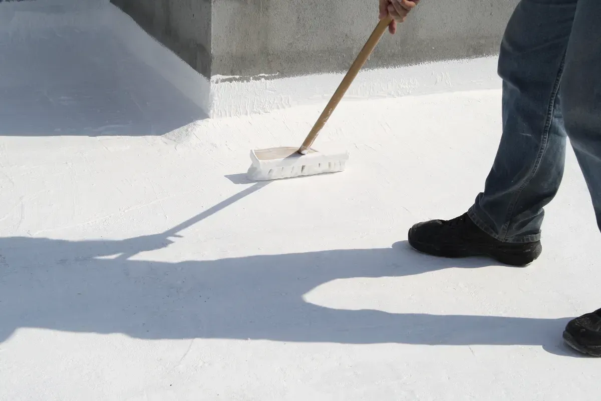 A person is painting a white surface with a broom.
