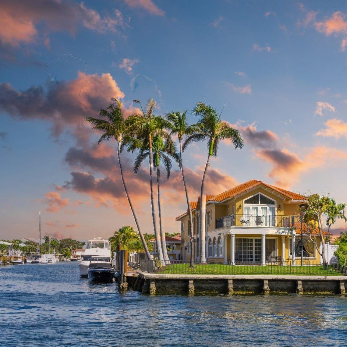 A house on a small island in the middle of a body of water surrounded by palm trees.